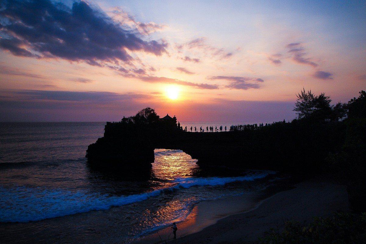 L'arche rocheuse du temple de Batu Bolong au coucher du soleil, couverte de visiteurs, à côté de Tanah Lot