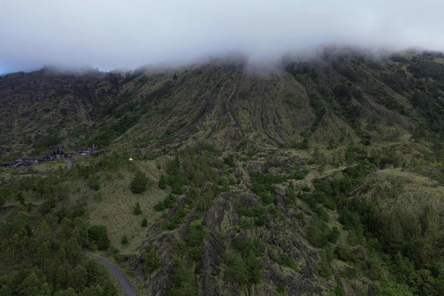 Le flanc du mont Batur couvert de nuages bas, avec un temple balinais sur la crête