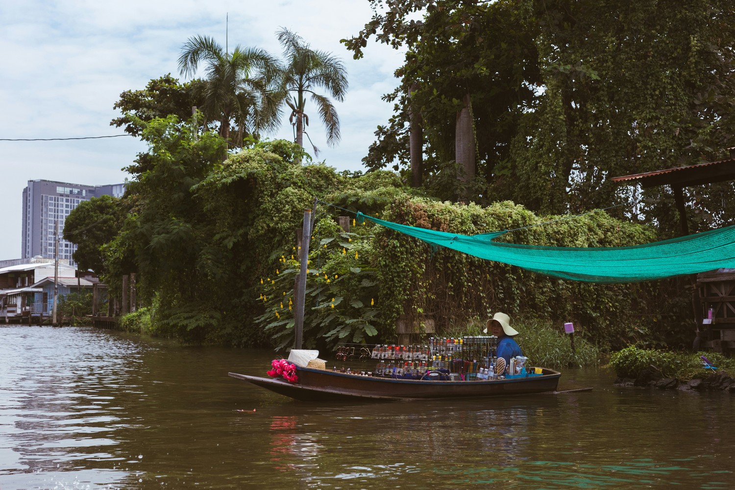 Vendeuse en barque sur un canal de Bangkok, immeubles de la ville en arrière-plan