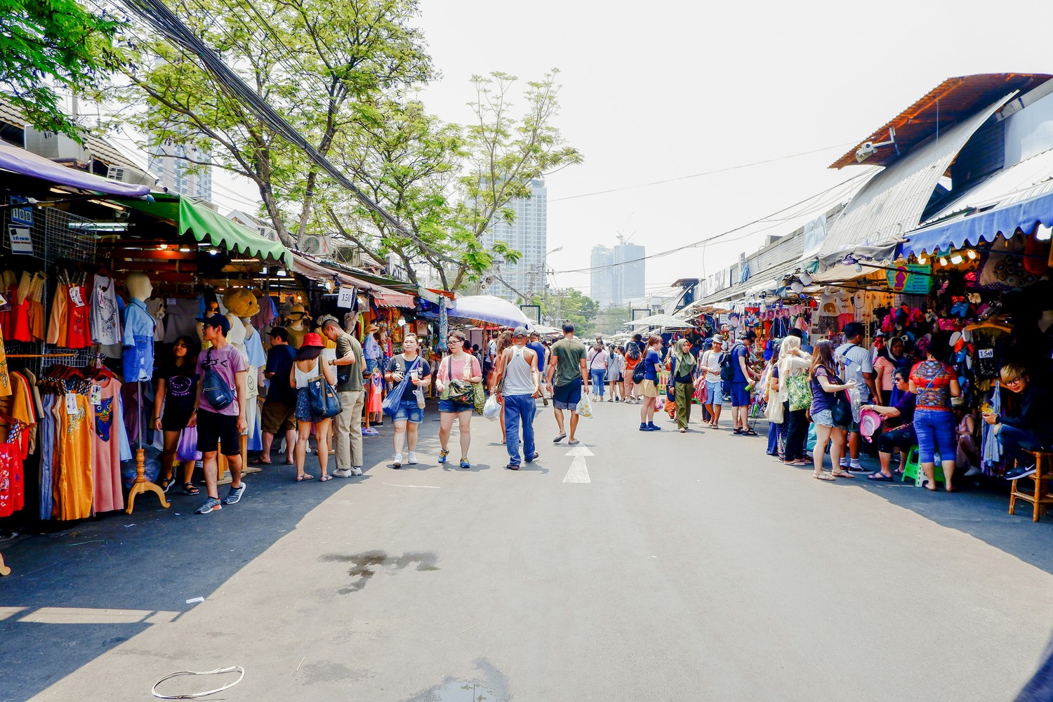 Allée principale du marché de Chatuchak bordée de stands de vêtements, en plein jour