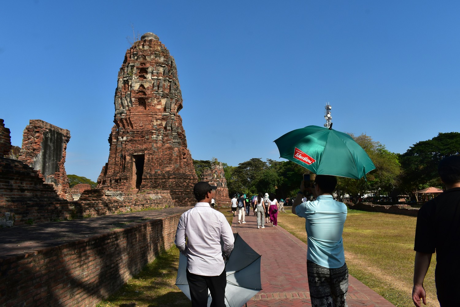 Visiteurs marchant sous des parasols devant un prang de brique à Ayutthaya