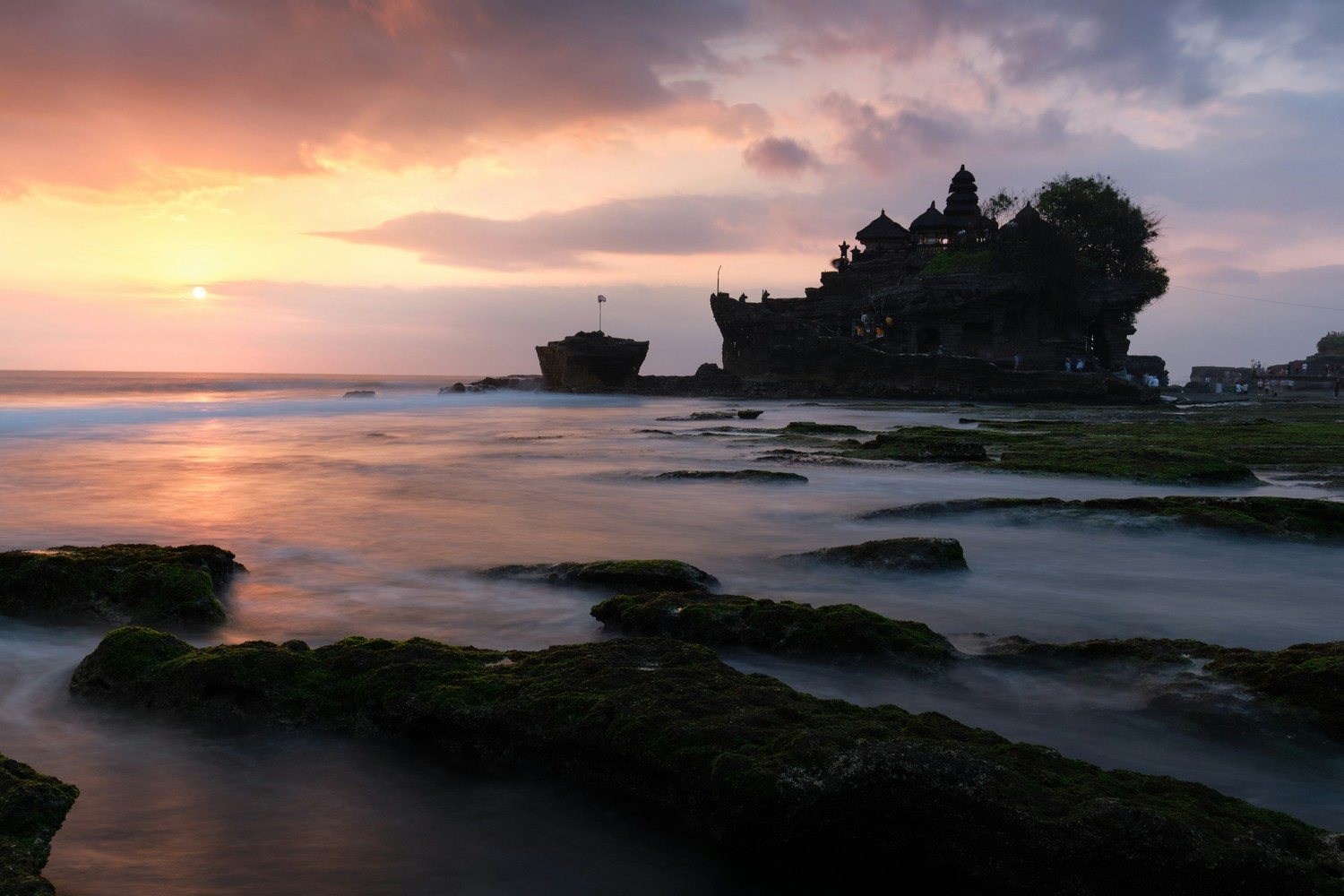 Le temple de Tanah Lot en silhouette au coucher du soleil, avec le platier rocheux découvert par la marée basse