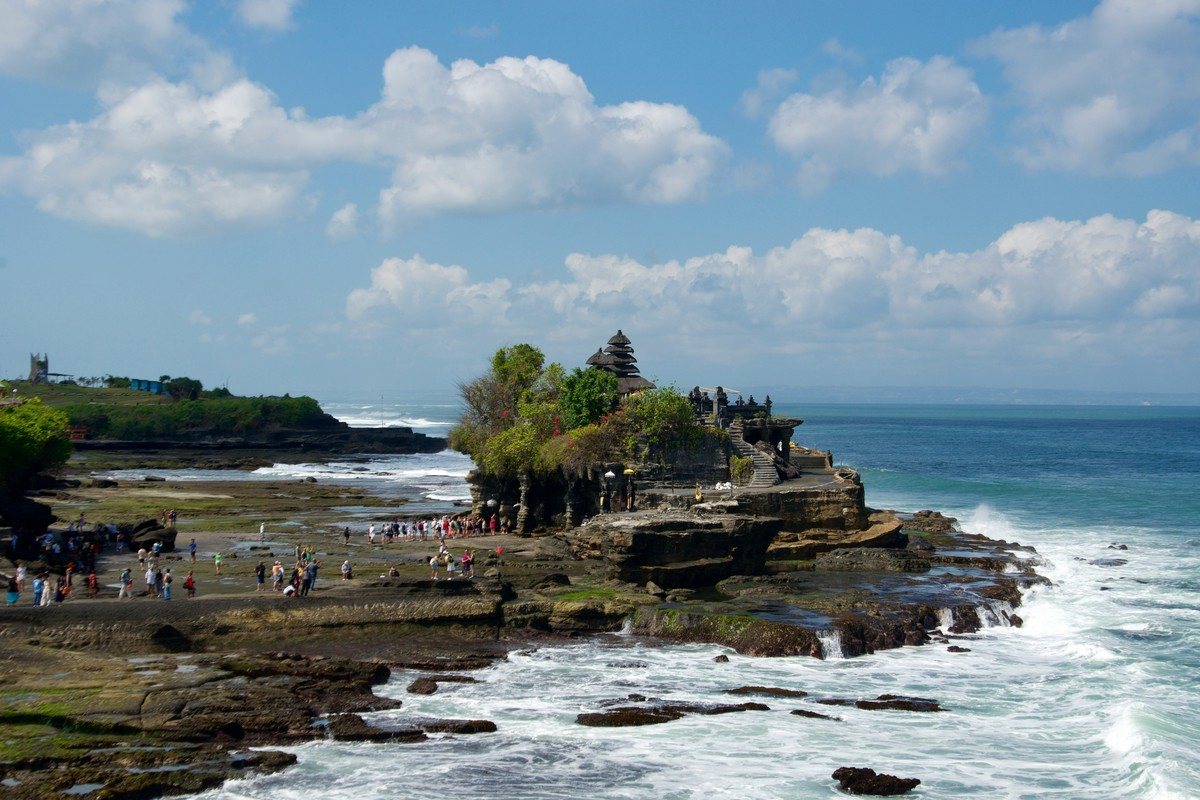 Des visiteurs marchent sur le platier rocheux jusqu'à la base du temple de Tanah Lot, à marée basse