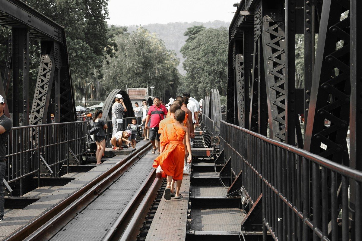 Visiteurs et un moine traversant à pied le pont de la rivière Kwaï entre les travées métalliques