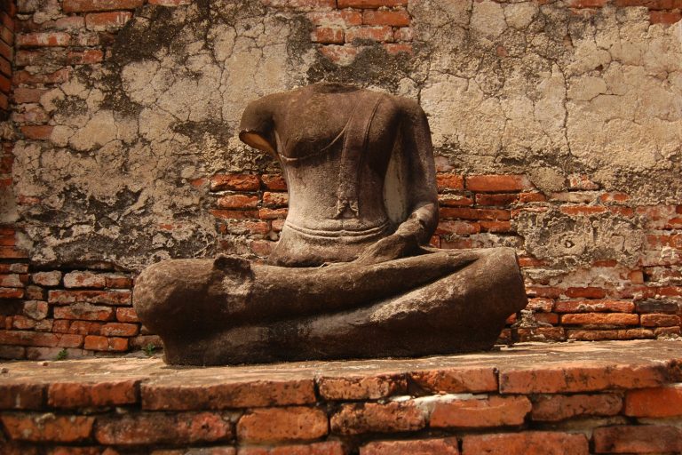 Statue de Bouddha décapitée adossée à un mur de brique, dans les ruines d'Ayutthaya