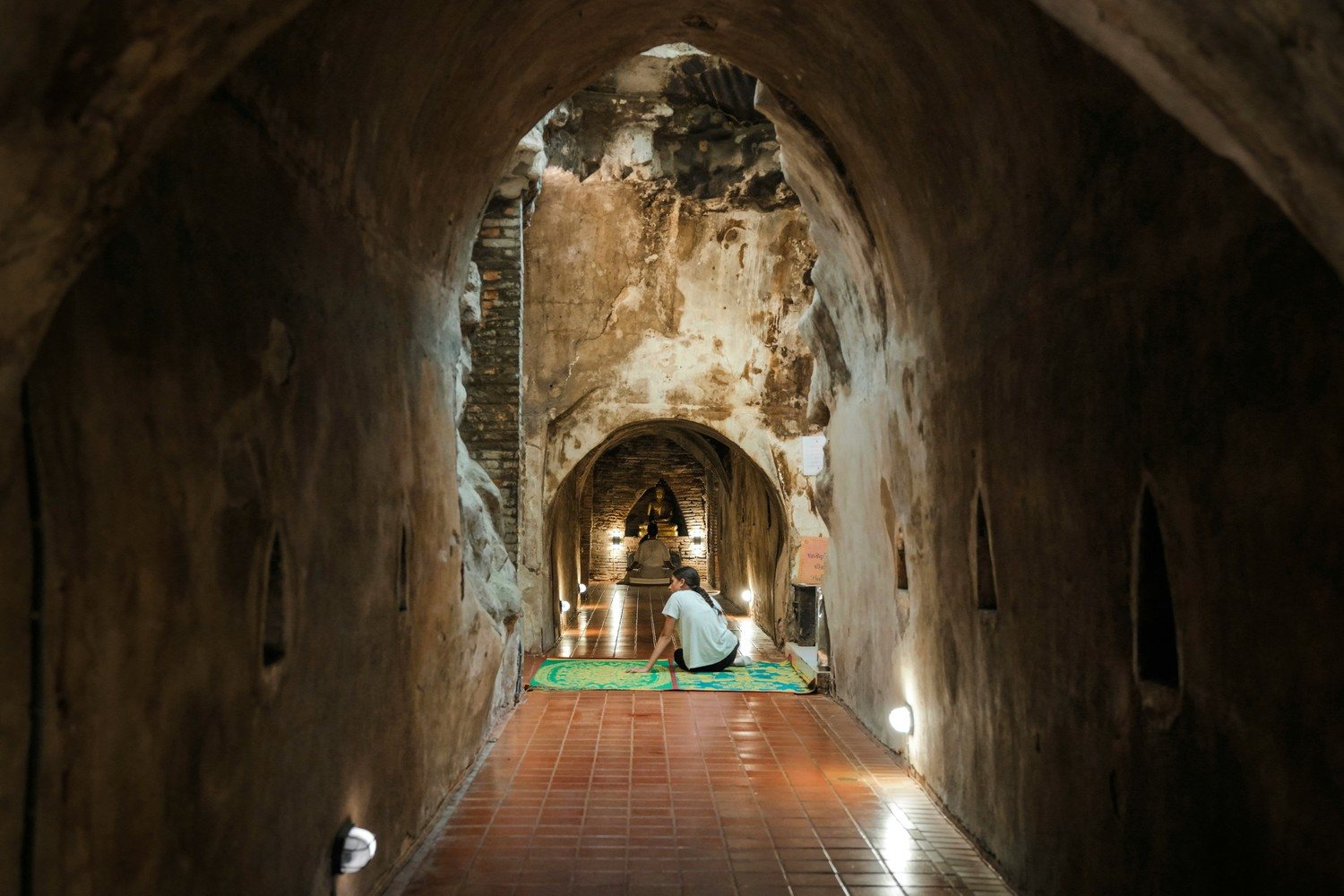 Un tunnel de brique vouté du Wat Umong avec un pratiquant assis devant un bouddha eclaire