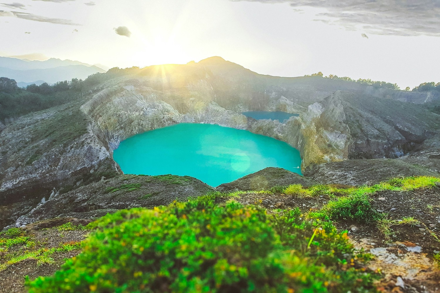 Deux lacs de cratère du Kelimutu au lever du soleil, l'un turquoise, l'autre sombre, cernés de parois rocheuses.