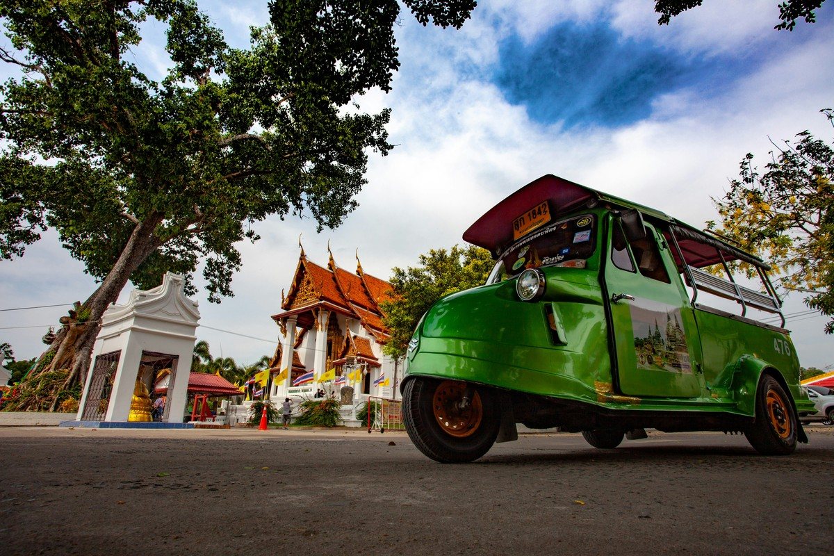 Tuk-tuk vert d'Ayutthaya, à la carrosserie arrondie, garé devant un temple